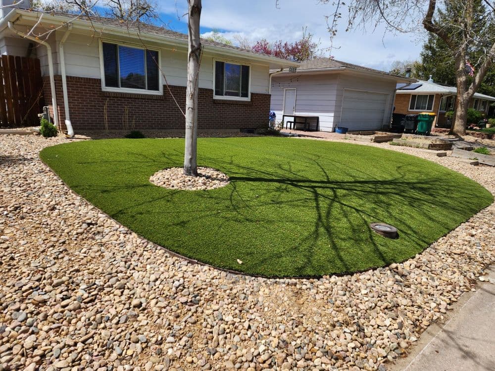 Artificial grass lawn installation featuring decorative rocks and a tree in a residential yard.