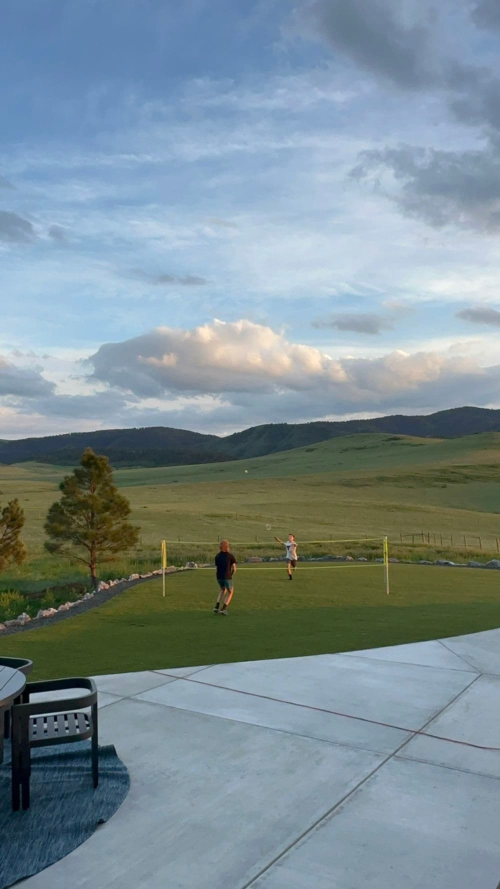 Children playing on a lawn against a backdrop of mountains and clouds at sunset.
