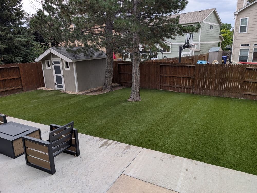 Lush green artificial grass yard with a shed and patio furniture in a residential area.