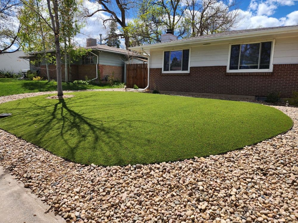 Lush artificial grass lawn with decorative rocks, sunny residential backyard setting.