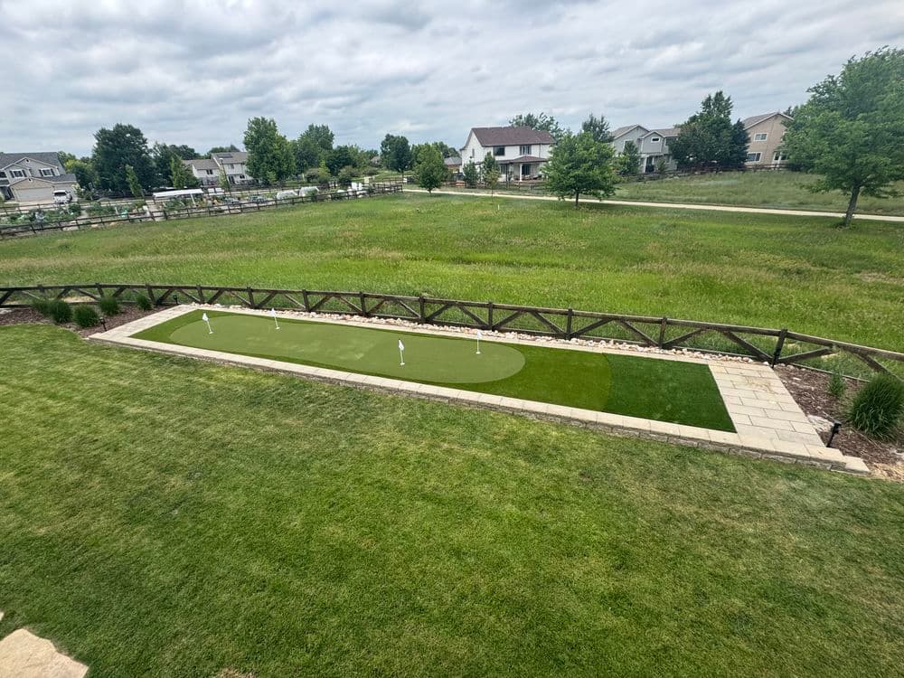 Backyard putting green with flags in a spacious lawn, surrounded by a wooden fence.