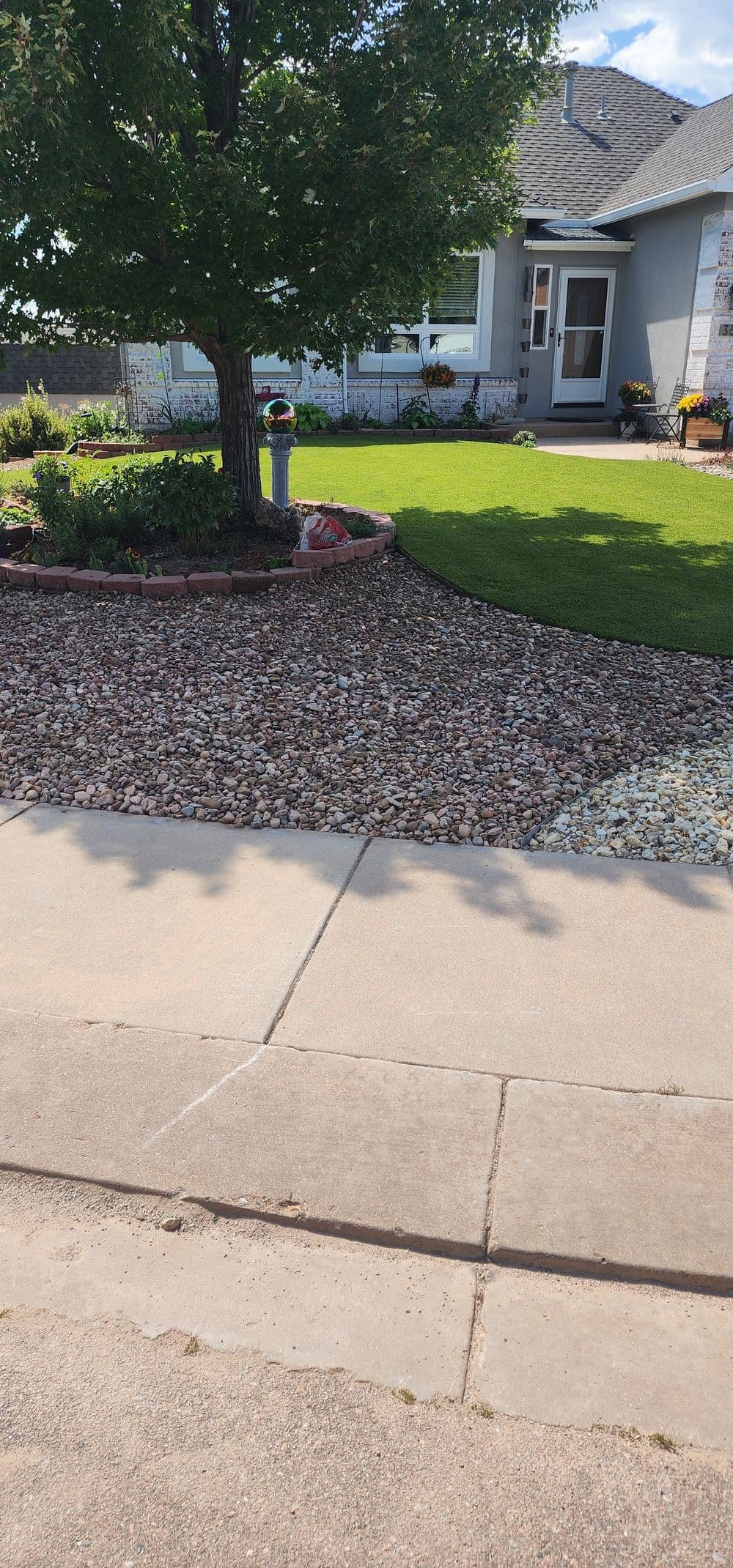 Lawn with decorative rocks and landscaping near a modern home with a tree in the front yard.