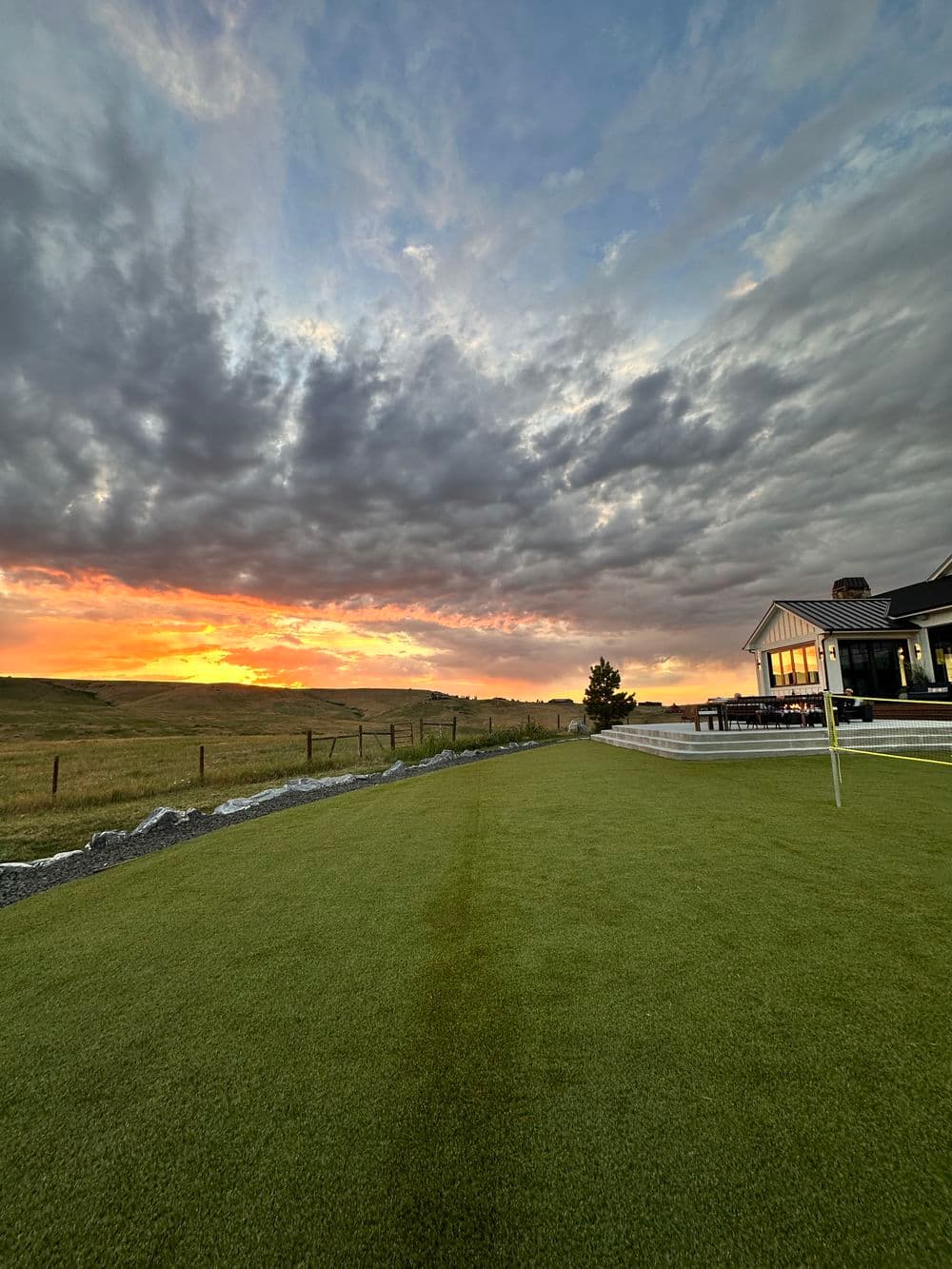Sunset over a green lawn with a house in the background, showcasing a serene landscape.