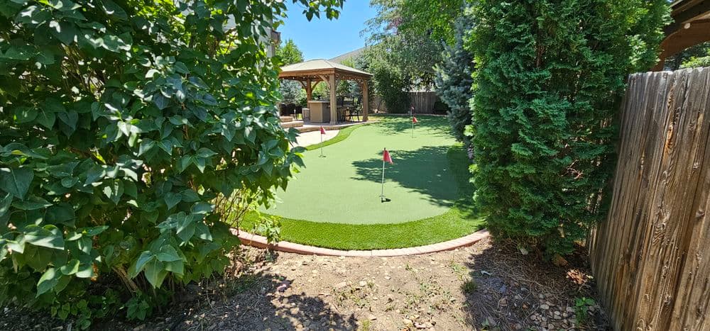Lush backyard putting green with gazebo and landscaped foliage. Perfect for golf practice.