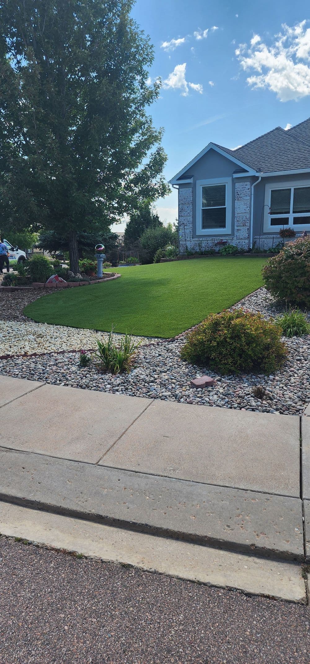 Lush green lawn and landscaped garden in front of a blue house on a sunny day.