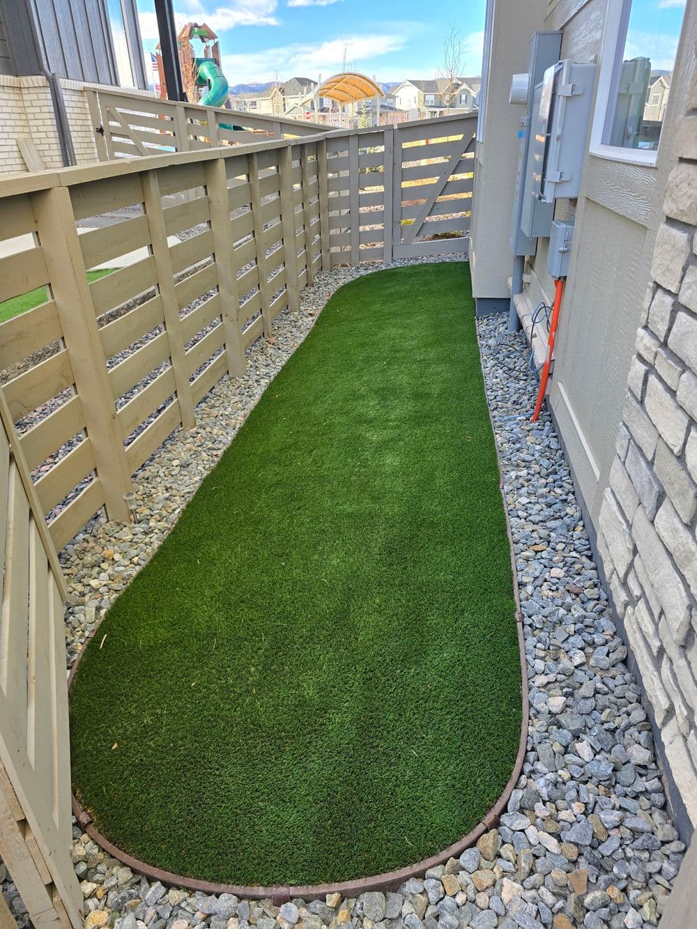 Artificial turf pathway alongside a fence in a residential area with gravel borders.