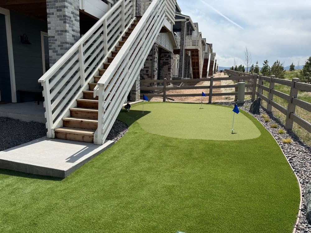 Mini golf area with putting green, blue flags, and wooden stairs in a residential setting.