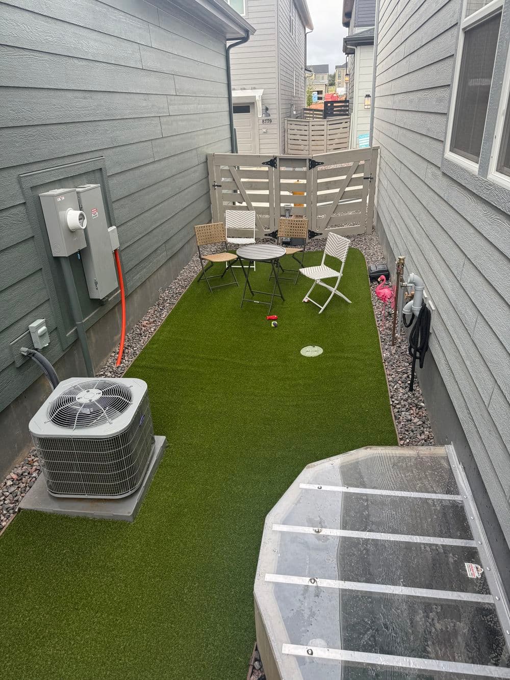 Artificial turf outdoor space with chairs, table, air conditioner, and gated entryway.