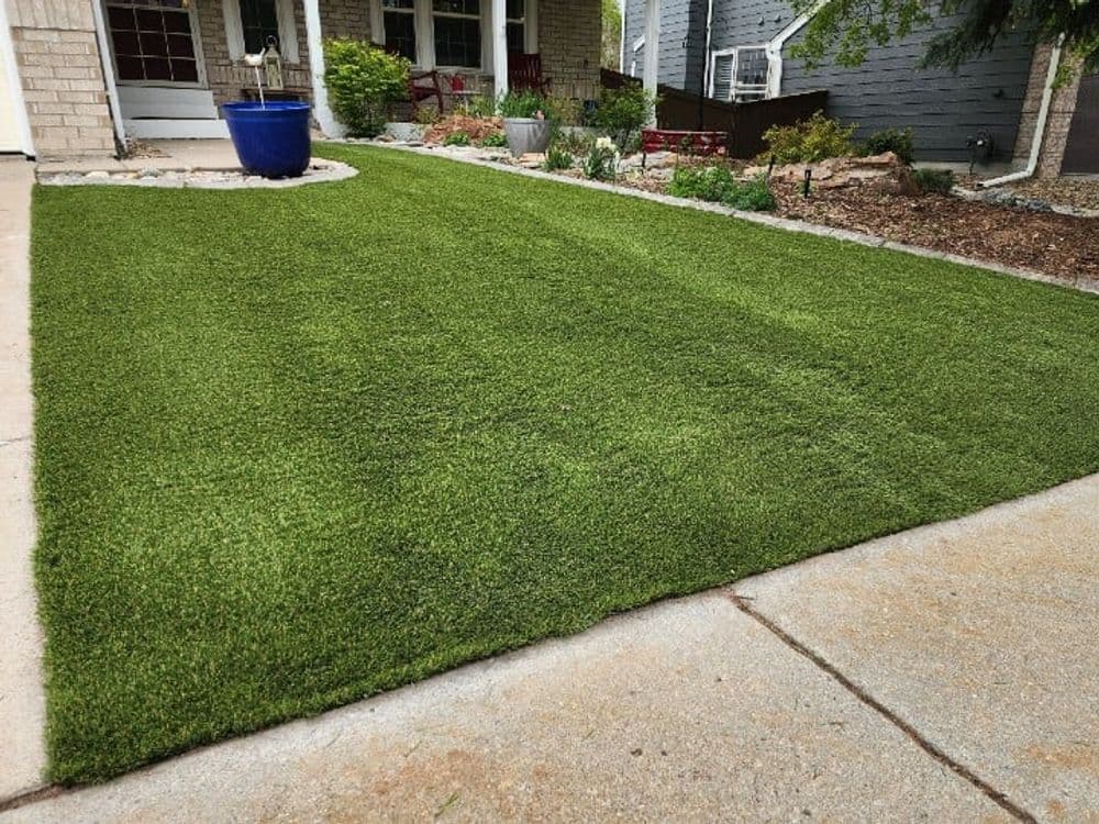 Verdant artificial turf lawn beside a stone walkway and garden in a suburban setting.