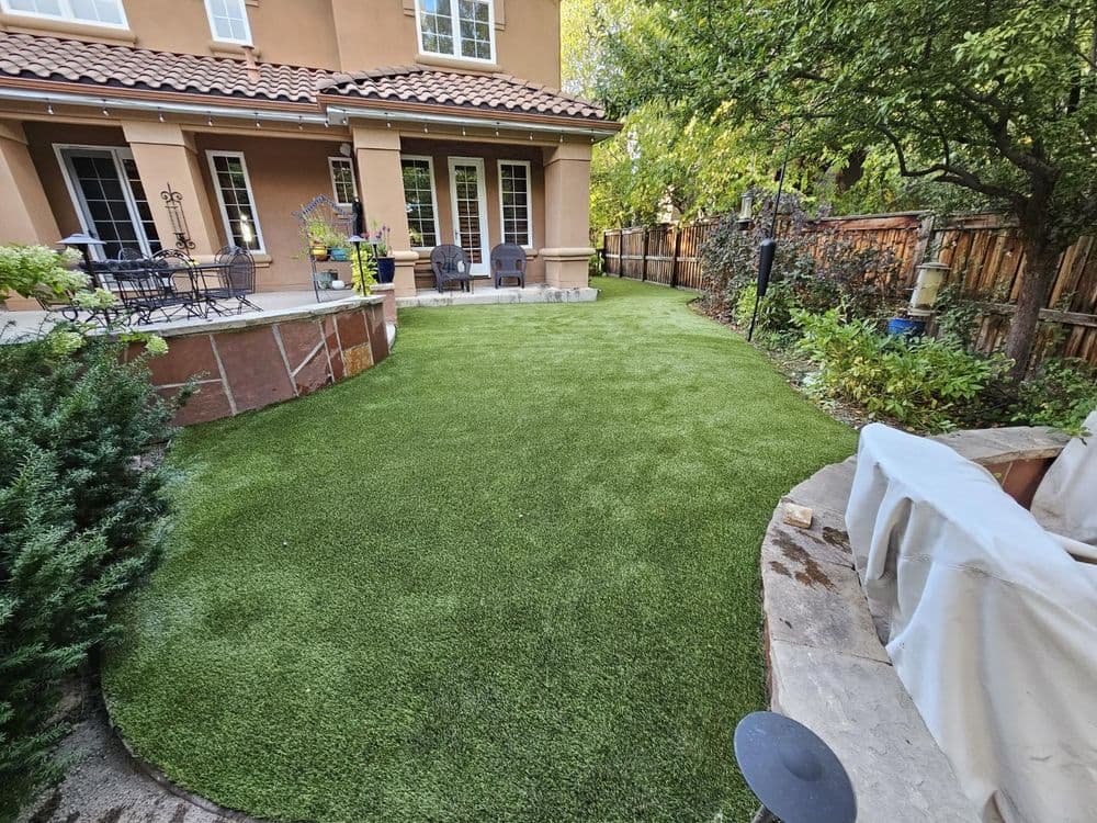 Lush green artificial turf backyard with patio seating and landscaped borders.